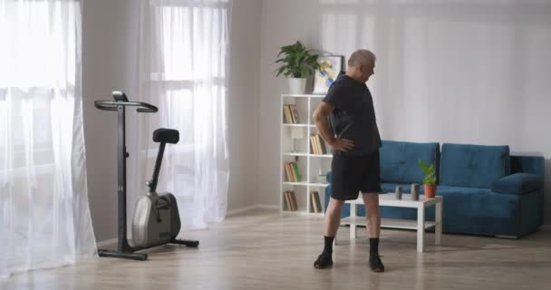 Anciano está haciendo ejercicios físicos en la sala de estar ligera en la mañana de fin de semana, estilo de vida saludable — Vídeos de Stock