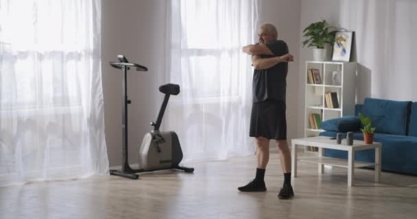 Középkorú felnőtt férfi egyedül edz a lakásában reggel, integet a kezével. — Stock videók
