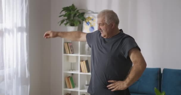 Пожилой человек делает гимнастику для суставов утром в доме, спортивная активность в среднем возрасте, поддержание физического состояния — стоковое видео