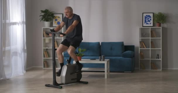 Sportos férfi edzés álló kerékpár otthon, kardio edzés tartása jó fizikai állapot középkorú — Stock videók