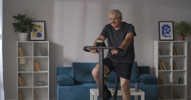 Remise en forme à domicile et mode de vie sain de l'homme d'âge moyen est l'entraînement sur vélo stationnaire dans l'appartement, entraînement cardio — Video