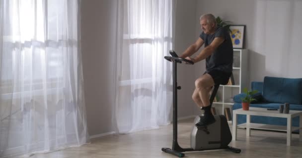 Treinamento de saúde em bicicleta estacionária, homem de meia-idade está girando pedais, exercício para respiração e sistema cardiovascular — Vídeo de Stock