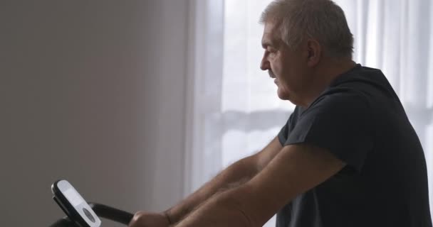 Sportieve activiteit tijdens zelfisolatie, mens traint met stationaire fiets thuis, portret — Stockvideo