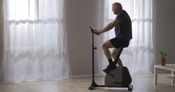 Entrenamiento en bicicleta estacionaria, hombre de mediana edad está girando pedales, ejercicio para la salud del sistema cardiovascular — Vídeo de stock