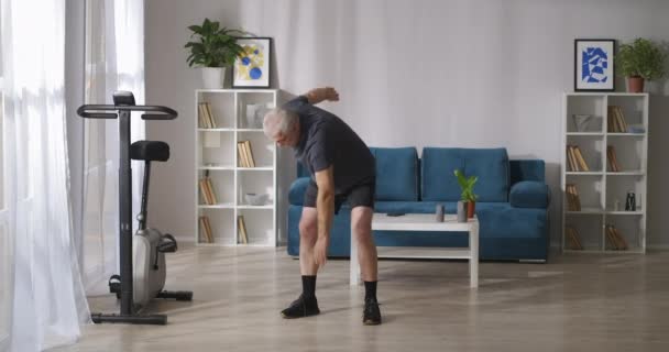Homem de meia-idade está fazendo inclinações durante a ginástica matinal, aquecimento do corpo e músculos de treinamento — Vídeo de Stock