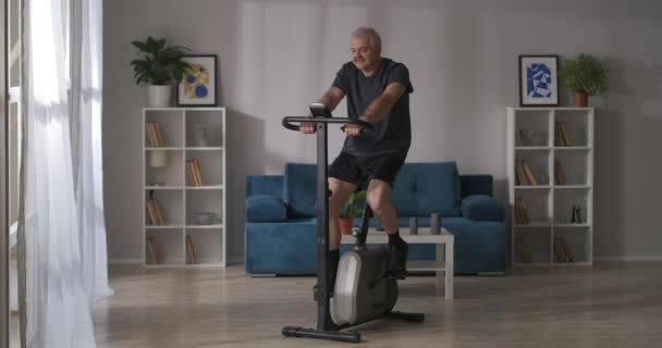 Nyugodt sportos középkorú férfi edzés forgó kerékpár a nappaliban, otthoni fitness, tartása fit — Stock videók