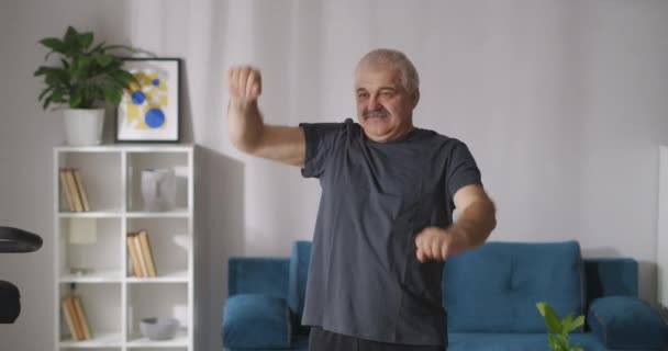 Zabawny człowiek z wąsami wykonuje ćwiczenia fizyczne w domu rano, podnosząc i opuszczając ręce — Wideo stockowe