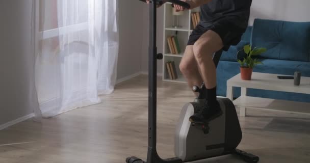 Formation à domicile sur vélo stationnaire, l'homme d'âge moyen tourne des pédales dans le salon, mode de vie sain — Video