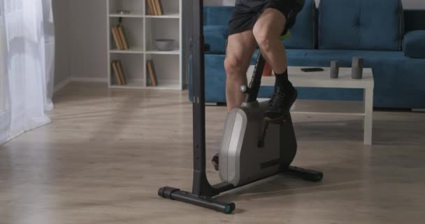 Homme sportif tourne pédales de vélo d'appartement à la maison, détails vue, l'entraînement et le maintien de sa condition physique — Video