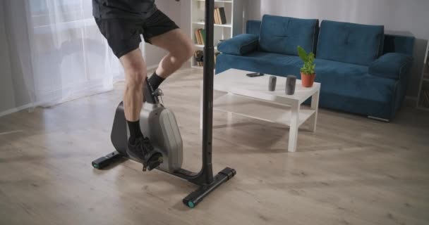 Jambes masculines sur vélo stationnaire dans le salon, l'homme adulte s'entraîne seul pour la santé et la bonne condition physique — Video