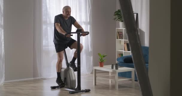 Zdrowy tryb życia i utrzymanie sprawności w średnim wieku, osoba trenuje na rowerze stacjonarnym w domu — Wideo stockowe