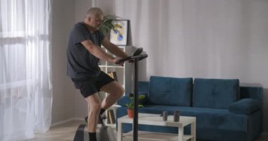 Formda ve fiziksel olarak iyi durumda olan orta yaşlı bir adam, staj bisikletiyle evde tek başına eğitim görüyor.