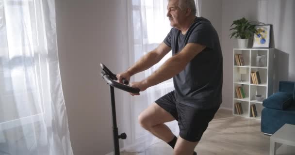 Bicicletta fissa per l'allenamento a casa, adulto dai capelli grigi sta utilizzando exercycle, pedali rotanti — Video Stock