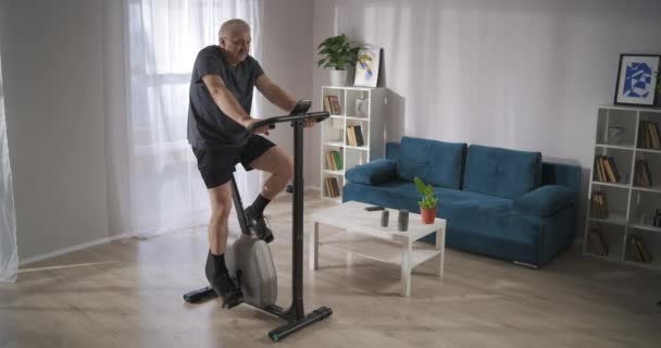 Hålla sig i form och hälsa för medelålders människor under självisolering, mannen tränar med exercycle — Stockvideo