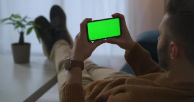 Yetişkin adam, yeşil ekran teknolojili modern akıllı telefon ekranına bakıyor. Rahatlatıcı ve görüntüleyici.