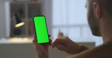 Genç adam modern cep telefonunu parmaklarıyla kaydırıyor, sosyal medyada haberleri okuyor, yeşil ekran teknolojisi