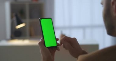 Adam evde yeşil ekranlı modern akıllı telefon kullanıyor. Sosyal ağ ve internet kullanıcısı, internette sörf yapıyor.