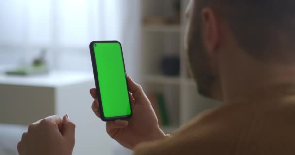 Видео чат в смартфоне с зеленым экраном, человек слушает и кивает головой, вид крупным планом через плечо — стоковое видео