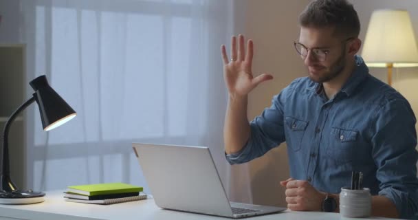 Vreugdevolle man begroet vrienden of collega 's via videogesprek in laptop, internetcommunicatie, in huis — Stockvideo