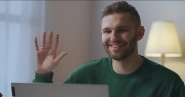 Веселый улыбающийся мужчина приветствует участников онлайн видео чата, машет рукой веб-камере, мужской портрет в гостиной — стоковое видео