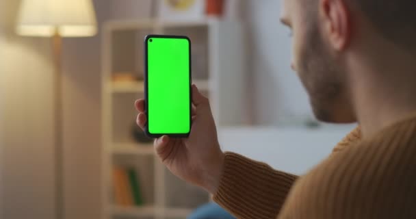 Videokonferens via smartphone, mannen håller gadget med grön skärm, sitter hemma, online-arbete eller vänliga möte, närbild — Stockvideo