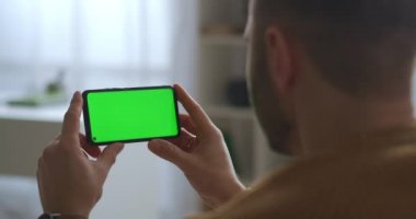 Adam yeşil ekrandaki cep telefonuna bakıyor, yatay olarak tutuyor, modern alet ve eğitim, iletişim ve eğlence uygulaması