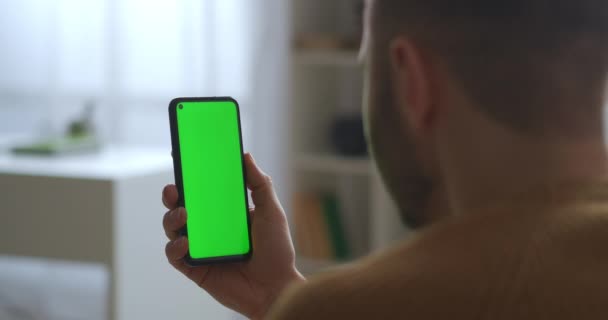 Guy is looking on green screen of smartphone, holding vertically, modern gadget and app, close seup view — стоковое видео