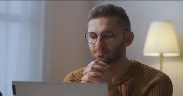 Jovem com óculos está ouvindo e vendo palestra ou discurso do participante da reunião on-line, sentado em casa escritório — Vídeo de Stock