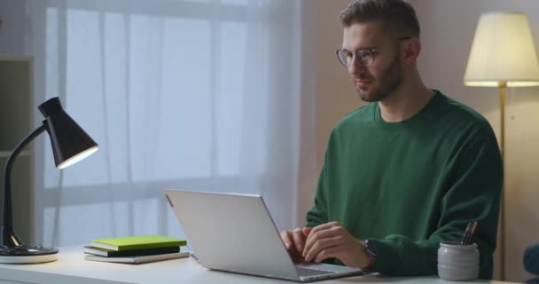 Mladý muž s brýlemi posílá zprávu v online chatu a čeká na odpověď, pomocí internetu na večer doma — Stock video