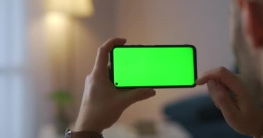 Erkek kullanıcı akıllı telefonda yeni uygulama kullanıyor, aygıtı yatay olarak tutuyor, montaj için yeşil ekran teknolojisi