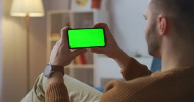 Görüntülü sohbetin katılımcısı akıllı telefon ekranına bakıyor ve yeşil ekranda kurgu için başını sallıyor