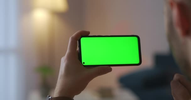 Hombre está viendo el cine en el cine en línea, utilizando el teléfono inteligente, pantalla de sensor táctil, tecnología de pantalla verde, entretenimiento en el hogar — Vídeos de Stock