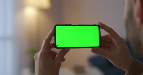 Hombre está sosteniendo el teléfono inteligente horizontalmente y ver vídeo, vista de cerca, pantalla verde para la tecnología de croma key — Vídeos de Stock