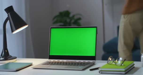 Laptop z wyświetlaczem klawiszy chroma na stole roboczym w salonie, człowiek włącza lampę podłogową i bierze okulary — Wideo stockowe