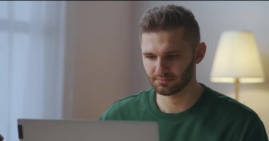 Yetişkin erkek internet kullanıcısı iş için dizüstü bilgisayarla gözlük takıyor, akşam oturma odasında bir adamın portresi.