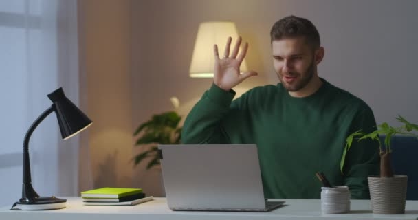 Handsome man is communicating by video chat by laptop, smiling and gesticulating looking at screen — Stock Video
