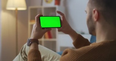 Erkek kullanıcı akıllı telefon ekranını dinliyor, yatay olarak tutuyor, apartmanda oturuyor, cep telefonları için yeni bir uygulama