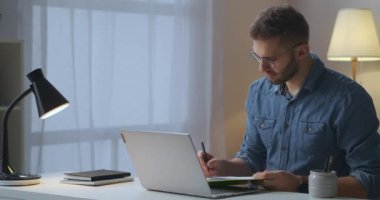 Yetişkin adam interlocutor dinlerken laptop üzerinden video görüşmesi yapıyor ve not alıyor, online iş toplantısı.