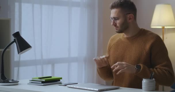 Muž zahajuje vzdálenou práci s notebookem doma, sedí u stolu a otevírá notebook, zapíná stolní lampu, píše na klávesnici — Stock video