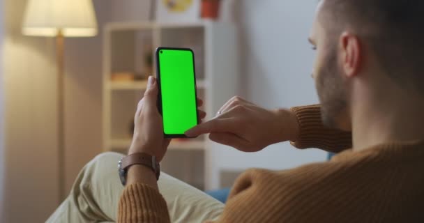 Чоловік купує в Інтернеті, замовляючи в додатку в смартфоні, витираючи пальцем, зелений екран на гаджеті — стокове відео