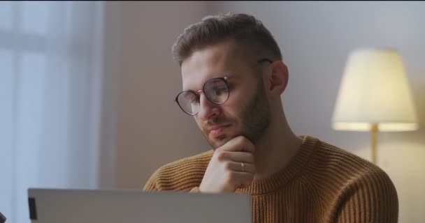 Langweiliger Mann mit Brille hört zu und schaut beim Online-Meeting mit Kollegen auf den Bildschirm, sitzt zu Hause und nickt. — Stockvideo