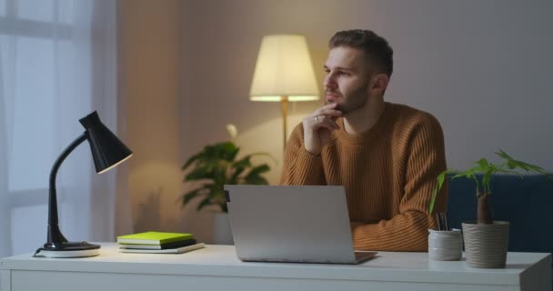 4.这个年轻人晚上穿着棕色的毛衣，带着笔记本电脑坐在桌前，在家里干活 — 图库视频影像
