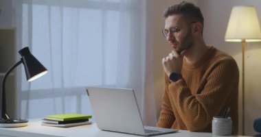 Yetişkin beyaz adam, eğitim ve eğlence için interneti kullanarak oturma odasında oturan defterin sergilendiği bir video izliyor.