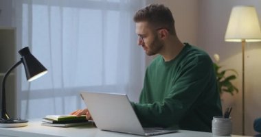 Yetişkin adam ana ofiste günlük planlamacı ve dizüstü bilgisayarla çalışıyor. Masada oturan klavyeyle yazı yazıyor.