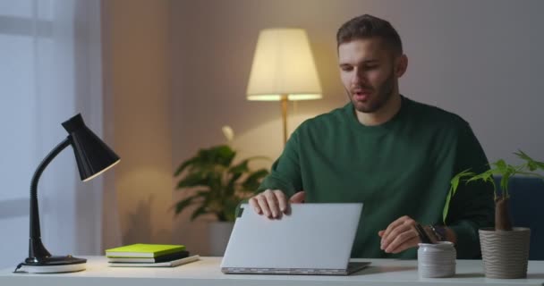 Trabalho remoto no escritório em casa à noite, homem cansado está fechando laptop e esfregando templos, excesso de trabalho e dor de cabeça — Vídeo de Stock