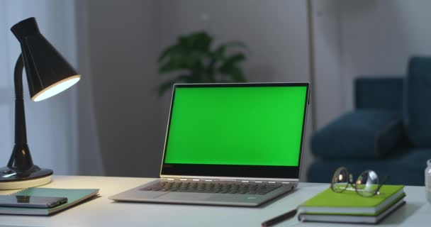 Laptop with green screen on working table in home office, man is turning on table and floor lamps in living room — Stock Video