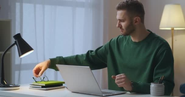 Muž si nasazuje brýle při práci s notebookem, ochraně vidění, dálkové práci z domova — Stock video
