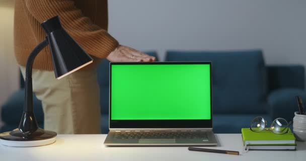 Mężczyzna zamyka laptop z zielonym ekranem w pokoju w godzinach wieczornych i wyłącza lampę, kończy pracę, widok na stół roboczy — Wideo stockowe