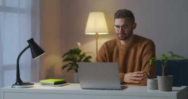 Video sohbetine katılan erkeğin portresi, başını sallıyor, dizüstü bilgisayarın görüntüsünü izliyor, evde oturuyor.