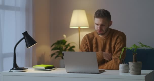 Zmęczony student zamyka laptopa po wykładzie online, siedzi w domu wieczorem, wyłączając lampę stołową — Wideo stockowe